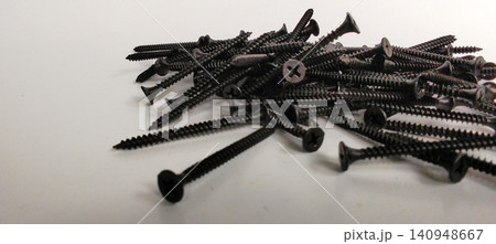 A pile of black drywall screws against a white background. A pile of black drywall screws against a white background. 140948667