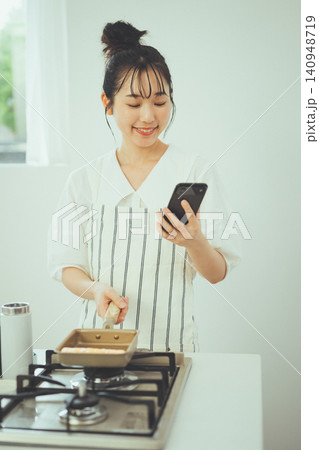 キッチンで料理しながらスマホを見て微笑む女性 キッチンで料理しながらスマホを見て微笑む女性 140948719