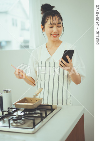 キッチンで料理しながらスマホを見て微笑む女性 キッチンで料理しながらスマホを見て微笑む女性 140948720