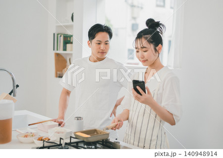キッチンでスマホのレシピを2人で確認しながら料理するカップル キッチンでスマホのレシピを2人で確認しながら料理するカップル 140948914