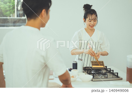 お弁当用の玉子焼きを焼く女性を見守る男性とキッチンの風景 お弁当用の玉子焼きを焼く女性を見守る男性とキッチンの風景 140949006