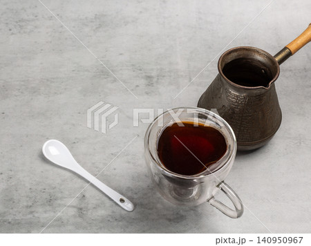 Cup of coffee, a spoon and a cezve on the kitchen table. Cup of coffee, a spoon and a cezve on the kitchen table. 140950967