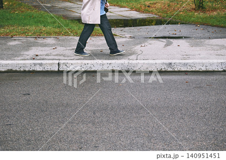 Legs of an ordinary woman in black jeans and sneakers walking along the sidewalk 140951451