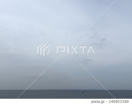曇り空の下に広がる静かな海と水平線に浮かぶ小さな船 140951580