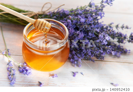 Honey dripping from dipper into jar with lavender flowers Honey dripping from dipper into jar with lavender flowers 140952410