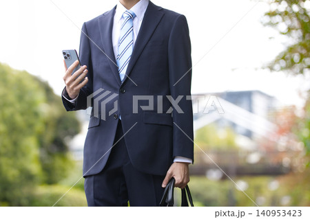 屋外でスマホを持つ20代のビジネスマン 屋外でスマホを持つ20代のビジネスマン 140953423