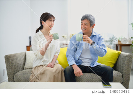 ソファに座ってコーヒーを飲む笑顔の60代の夫婦 ソファに座ってコーヒーを飲む笑顔の60代の夫婦 140953452
