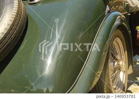 Close-up of a vintage green car's rear fender and spare tire. Detailed view of the curved fender, wire wheel, and external spare tire on a classic automobile, showcasing its aged charm and design 140953781