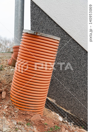 A thick drainage pipe protruding from the ground near a house, part of the water management system, surrounded by soil and construction elements. High quality photo A thick drainage pipe protruding from the ground near a house, part of the water management system, surrounded by soil and construction elements. High quality photo 140953869