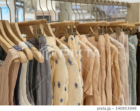 Pleated pastel color clothes hanging on wooden hangers in shop Pleated pastel color clothes hanging on wooden hangers in shop 140953949