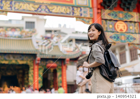 Young woman backpack camera smiling outdoor temple travel sightseeing Asian casual joyful exploring cultural tourism architecture city adventure holiday vacation urban traditional landmark 140954321