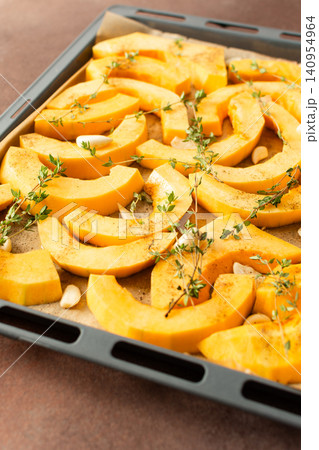 Butternut squash slices are arranged on a tray with herbs and garlic, ready for roasting. This is part of a cooking process in a kitchen setting Butternut squash slices are arranged on a tray with herbs and garlic, ready for roasting. This is part of a cooking process in a kitchen setting 140954964