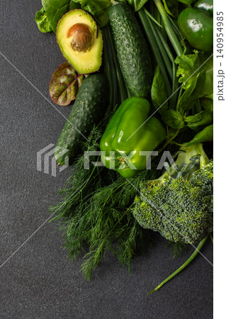 A variety of fresh green vegetables is neatly arranged on a dark surface, showcasing cucumbers, bell pepper, avocado, broccoli, and various leafy greens, healthy eating for a nutritious salad A variety of fresh green vegetables is neatly arranged on a dark surface, showcasing cucumbers, bell pepper, avocado, broccoli, and various leafy greens, healthy eating for a nutritious salad 140954985