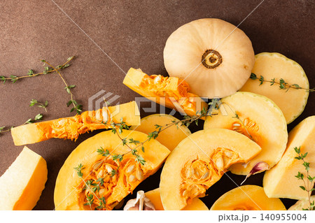Yellow squash sliced into pieces is placed on a brown surface. Garlic cloves and fresh thyme are nearby, adding texture and color to the arrangement of vegetables Yellow squash sliced into pieces is placed on a brown surface. Garlic cloves and fresh thyme are nearby, adding texture and color to the arrangement of vegetables 140955004