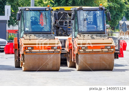 Construction vehicles work together on a road project in a busy urban area during the daytime 140955124