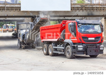 Construction workers operate machinery at a site in a city during the day as they remove asphalt and prepare for new pavement Construction workers operate machinery at a site in a city during the day as they remove asphalt and prepare for new pavement 140955858