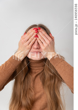 Young woman hiding her face with hands, creating a sense of secrecy and privacy while depicting a moment of shyness or playful concealment on a plain background Young woman hiding her face with hands, creating a sense of secrecy and privacy while depicting a moment of shyness or playful concealment on a plain background 140956598