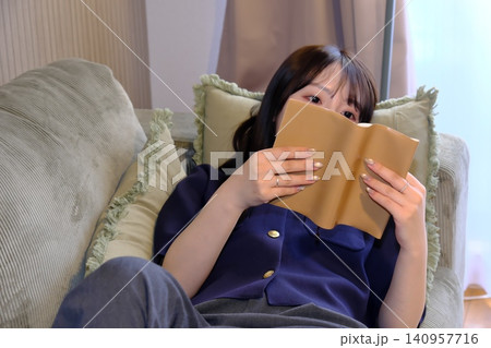 癒しの「自分時間」。ソファで寝ころびながら読書に没頭する女性の穏やかなライフスタイルシーン 140957716