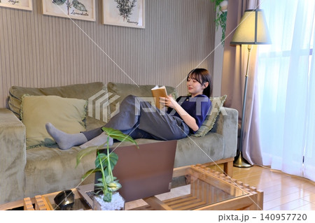 癒しの「自分時間」。ソファで寝ころびながら読書に没頭する女性の穏やかなライフスタイルシーン 癒しの「自分時間」。ソファで寝ころびながら読書に没頭する女性の穏やかなライフスタイルシーン 140957720