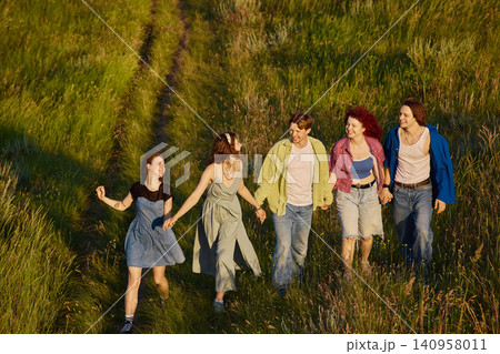 Friends holding hands while walking through tall grass at sunset. 140958011