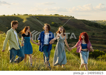 Friends laughing and walking across countryside meadow at golden hour. Friends laughing and walking across countryside meadow at golden hour. 140958023