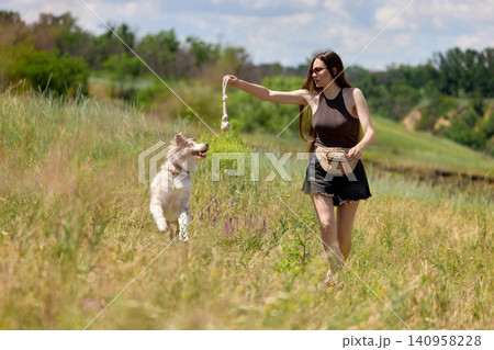 Woman playing with dog toy in open countryside field. 140958228