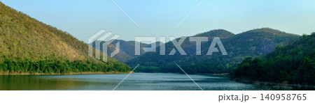 Panoramic view of a peaceful lake surrounded by lush green mountains and clear blue sky Panoramic view of a peaceful lake surrounded by lush green mountains and clear blue sky 140958765