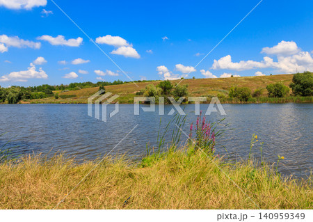 Summer landscape with beautiful lake, green meadows, hills, trees and blue sky Summer landscape with beautiful lake, green meadows, hills, trees and blue sky 140959349