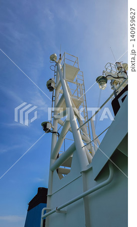 Vertical low angle shot of a white metal industrial ship mast with navigation lights and ladders on a commercial vessel superstructure under a clear blue sky 140959627