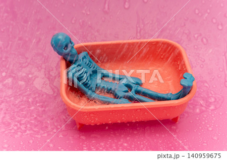 Skeleton toy floats in orange tub under water spray on pink surface Skeleton toy floats in orange tub under water spray on pink surface 140959675