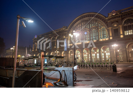 Turin, piedmont, italy. November 20, 2024. Porta nuova station in turin featuring its historic architecture illuminated at dusk with street lamps and shared bicycles Turin, piedmont, italy. November 20, 2024. Porta nuova station in turin featuring its historic architecture illuminated at dusk with street lamps and shared bicycles 140959812