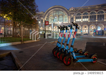 Turin, piedmont, italy. November 20, 2024. Row of electric scooters standing on a sidewalk in front of turin porta nuova train station, offering sustainable city transport Turin, piedmont, italy. November 20, 2024. Row of electric scooters standing on a sidewalk in front of turin porta nuova train station, offering sustainable city transport 140959815
