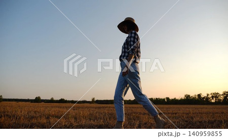 Adult agronomist in straw hat walking among barley plantation at dusk. Female farmer going through wheat meadow at sunset. Beautiful scenic landscape. Concept of agricultural business. Slow motion Adult agronomist in straw hat walking among barley plantation at dusk. Female farmer going through wheat meadow at sunset. Beautiful scenic landscape. Concept of agricultural business. Slow motion 140959855