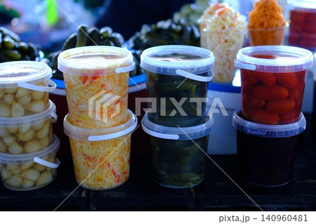 pickled tomatoes mushrooms cucumbers in buckets sauerkraut at market. Fresh sauerkraut with carrot shreds displayed in transparent plastic container on market counter, market vendor presenting pickled tomatoes mushrooms cucumbers in buckets sauerkraut at market. Fresh sauerkraut with carrot shreds displayed in transparent plastic container on market counter, market vendor presenting 140960481
