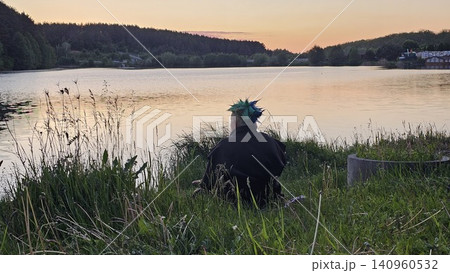 Person relaxing by sparkling lakeshore surrounded by reeds on bright sunny day in peaceful naturePerson sitting by quiet lake at sunset enjoying peaceful evening landscape and reflection 140960532