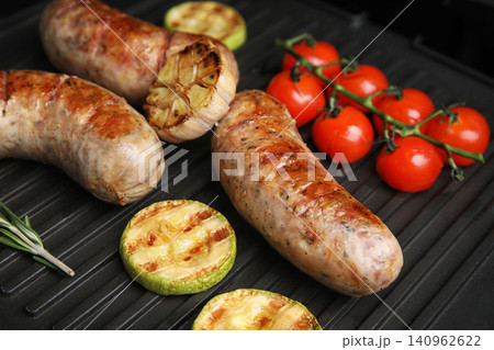 Cooking delicious fresh sausages with vegetables on modern grill 140962622