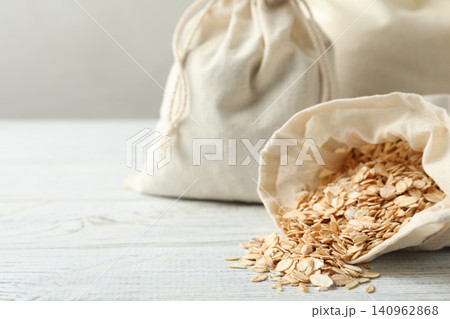 Cotton eco bags with oat flakes on white wooden table, closeup. Space for text Cotton eco bags with oat flakes on white wooden table, closeup. Space for text 140962868