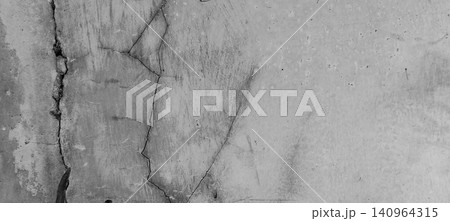 The texture of a cracked and weathered concrete wall set against a background of a worn-looking cement surface. 140964315