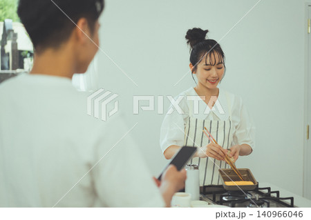 男性に見守られながら玉子焼きを丁寧に巻く女性のキッチンシーン 男性に見守られながら玉子焼きを丁寧に巻く女性のキッチンシーン 140966046