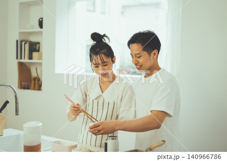 キッチンで並んで弁当のおかずを詰めながら微笑み合うカップルの朝 キッチンで並んで弁当のおかずを詰めながら微笑み合うカップルの朝 140966786