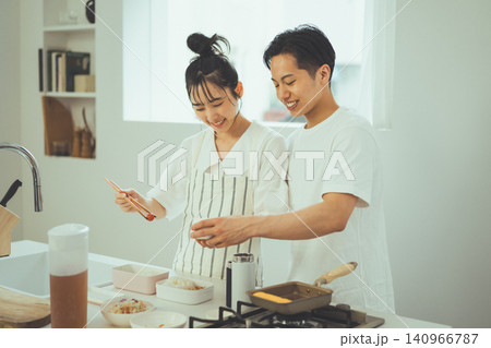 キッチンで並んで笑顔でお弁当作りをするカップルと玉子焼き器 キッチンで並んで笑顔でお弁当作りをするカップルと玉子焼き器 140966787