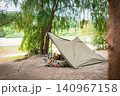 静かな水辺の森に溶け込むミリタリーパップテントと並べられたお洒落なキャンプ道具 静かな水辺の森に溶け込むミリタリーパップテントと並べられたお洒落なキャンプ道具 140967158