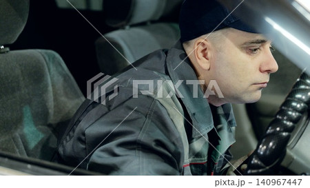 Skilled mechanic in baseball cap testing vehicle after servicing, gripping steering wheel inside automotive workshop Skilled mechanic in baseball cap testing vehicle after servicing, gripping steering wheel inside automotive workshop 140967447