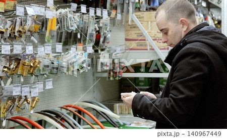 Plumber carefully choosing plumbing parts, reading label on small plastic fitting, standing in hardware store, in front of shelves with various equipment Plumber carefully choosing plumbing parts, reading label on small plastic fitting, standing in hardware store, in front of shelves with various equipment 140967449