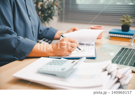 Professional writing on financial report with laptop, calculator, and papers on office desk, showing accounting review, budget planning, audit pressure, business data, and productivity. 140968157