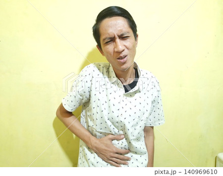 Young Asian Man Feeling Stressed with Headache Against Yellow Wall Young Asian Man Feeling Stressed with Headache Against Yellow Wall 140969610