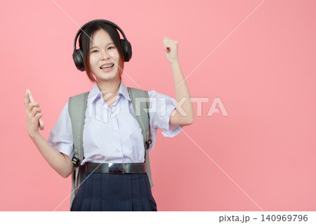 Student in uniform listening music from Smartphone with Headphone studio isolated pink background. 140969796