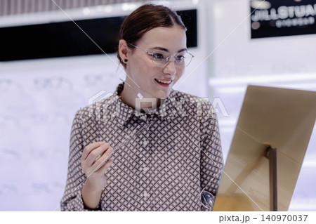 Woman trying on eyeglasses in optical store, happy customer shopping for new eyewear 140970037