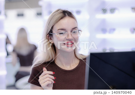 Young woman trying on eyeglasses in optical store, happy customer shopping for new eyewear Young woman trying on eyeglasses in optical store, happy customer shopping for new eyewear 140970040