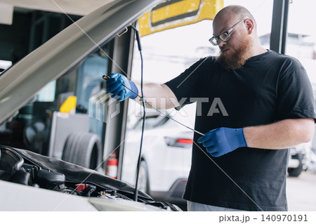 Garage Mechanic worker in auto service center working check and change engine oil under hood. 140970191